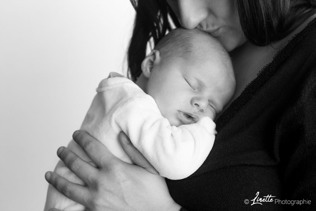 Photo de naissance E. par Linette Photographie. Photographie en noir et blanc d'un nouveau né endormi dans les bras de sa mère.